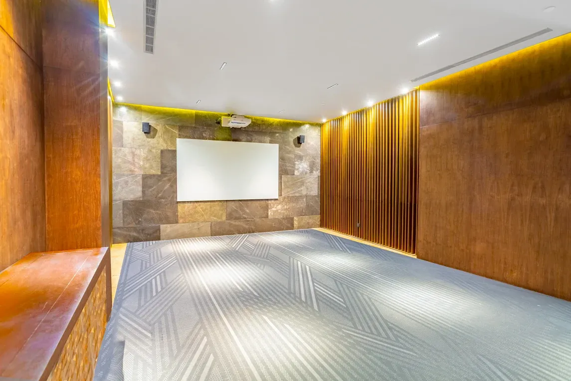 Modern conference room with projector and screen, wood paneling, and geometric carpet. The Fives Corpo