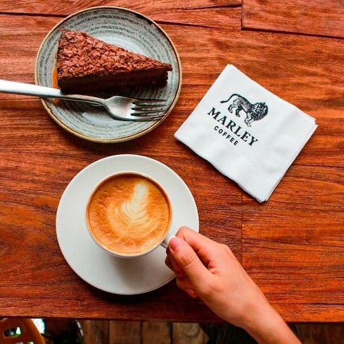 a person holding a cup of coffee next to a marley coffee napkin