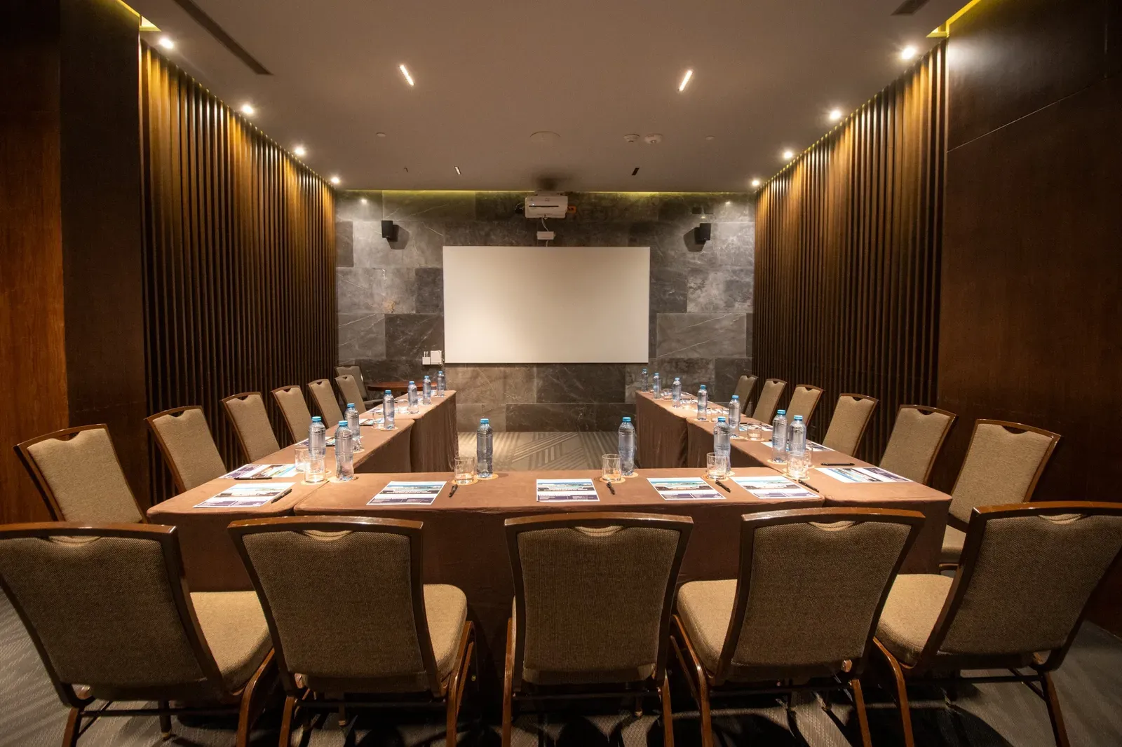 Modern conference room with U-shaped tables, chairs, projector, and The Fives Corpo screen.