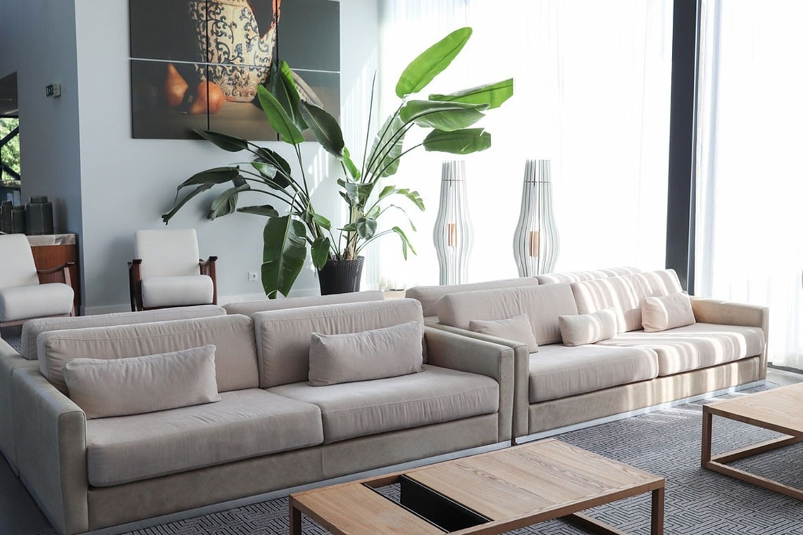 Lounge moderno com sofás bege e plantas grandes no Monchique Resort & SPA by Flagworld Hotels.
