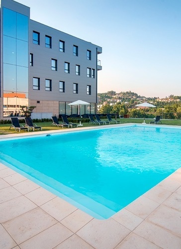 a large swimming pool surrounded by chairs and umbrellas in front of a building