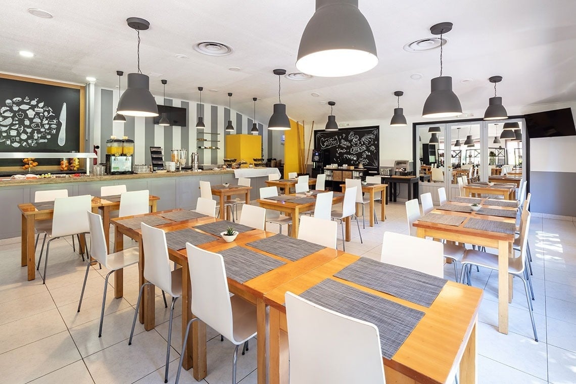 Salão de café da manhã do Campanile Setúbal com mesas arrumadas e luminárias modernas.
