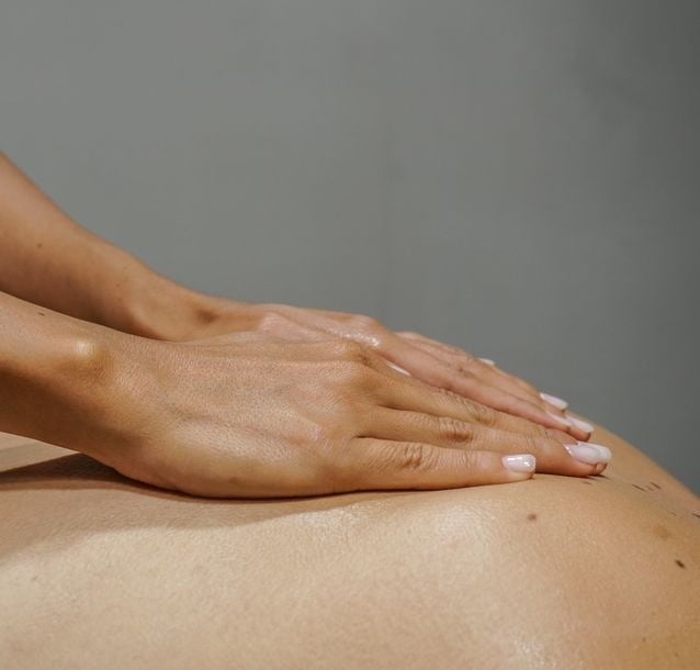 Duas mãos realizam uma massagem nas costas de uma pessoa.