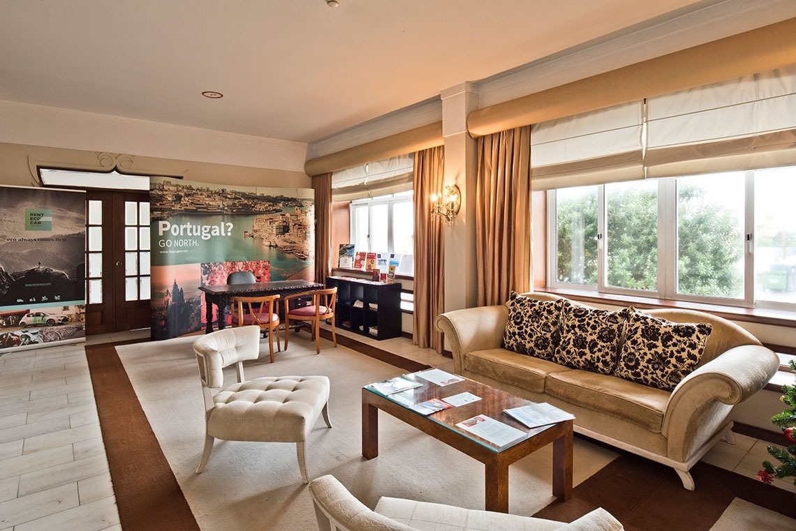 Elegant lobby of Lam Hotel Porto-Gaia with plush seating and promotional banners. Official website.