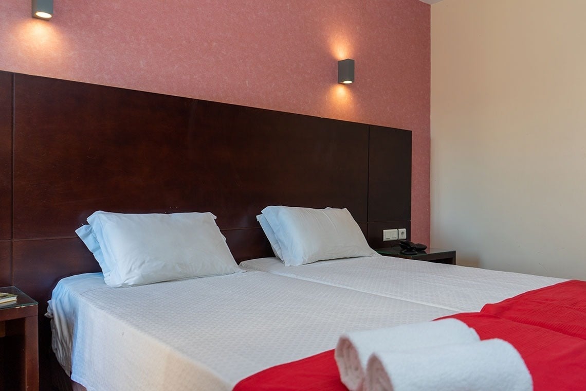 Comfortable twin beds with white linens and red throws at Flag Hotel Barcelos.