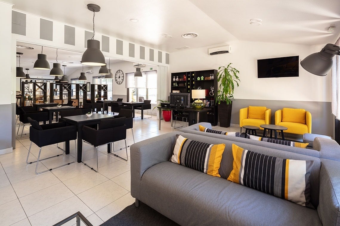 Sala de estar moderna com sofás cinza, cadeiras amarelas e área de jantar, no Campanile Setúbal.
