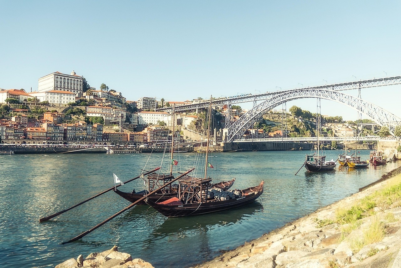 um grupo de barcos está ancorado em um rio com uma ponte ao fundo .