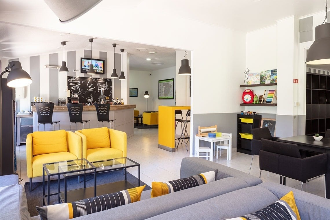 Lounge moderno com sofás amarelos e cinza, bar e área infantil no Campanile Setúbal.
