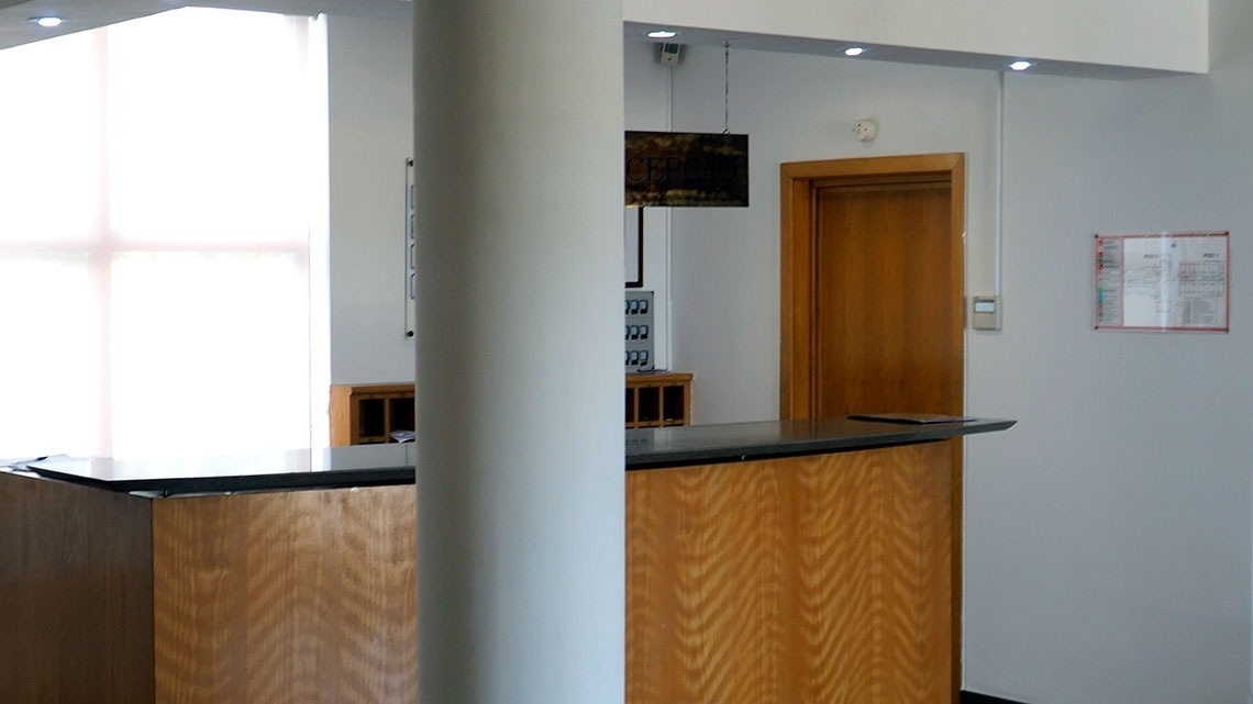 Recepção moderna do Flag Hotel Porto-Maia, com balcão de madeira, porta e quadro de avisos.