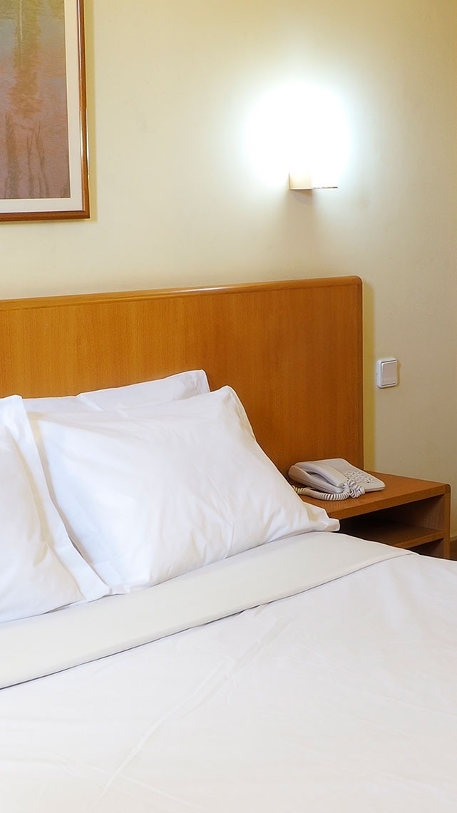 Cama de hotel branca arrumada com telefone e quadro no quarto. Flag Hotel Porto-Maia | Site Oficial.