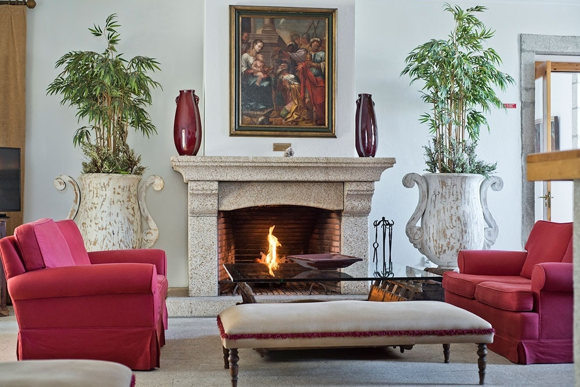 Salón acogedor con chimenea, sofás rojos y plantas. Lam Hotel Convento do Desagravo | Web oficial.
