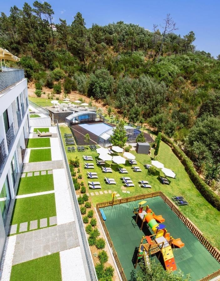 Monchique Resort & SPA: Piscina, playground e espreguiçadeiras rodeadas por natureza exuberante.