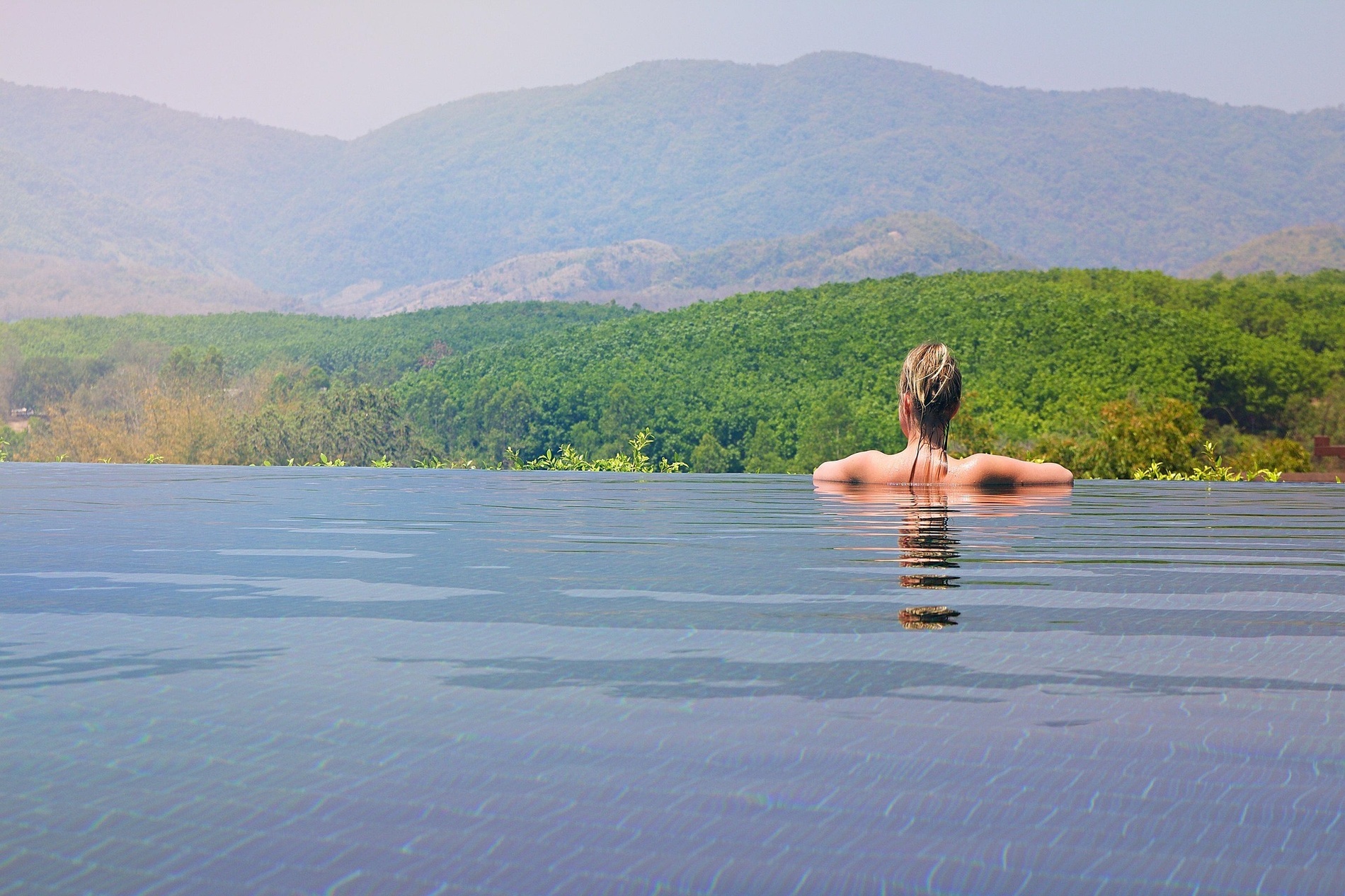 una mujer flota en una piscina infinita con montañas en el fondo