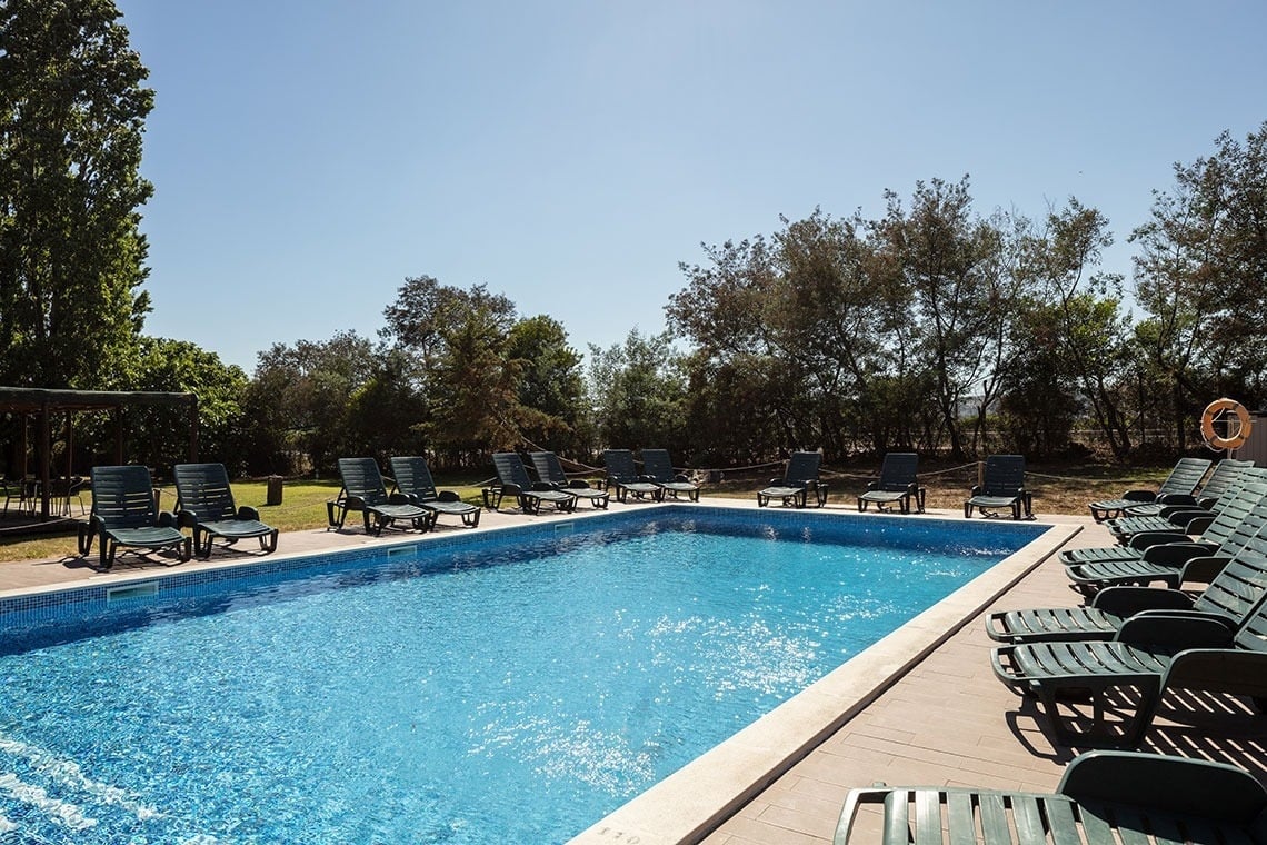Piscina exterior do Campanile Setúbal | Website oficial, com espreguiçadeiras e rodeada de árvores.
