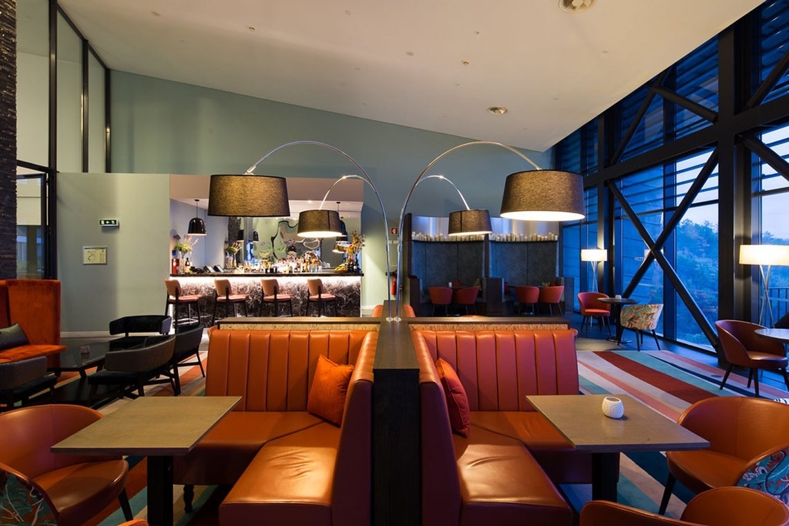 Salão moderno com sofás laranja, bar e vista para a natureza no Monchique Resort & SPA