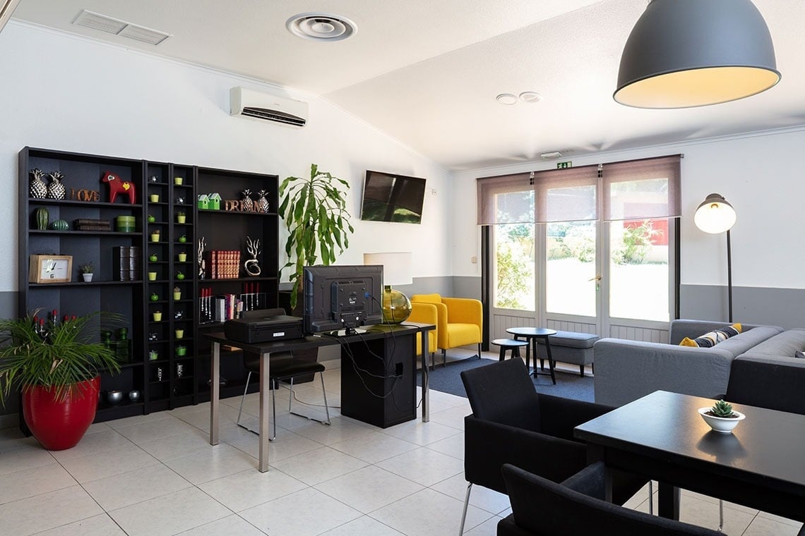 Sala de estar moderna Campanile Setúbal | Website oficial, com poltronas amarelas, sofás cinzas e área de trabalho.