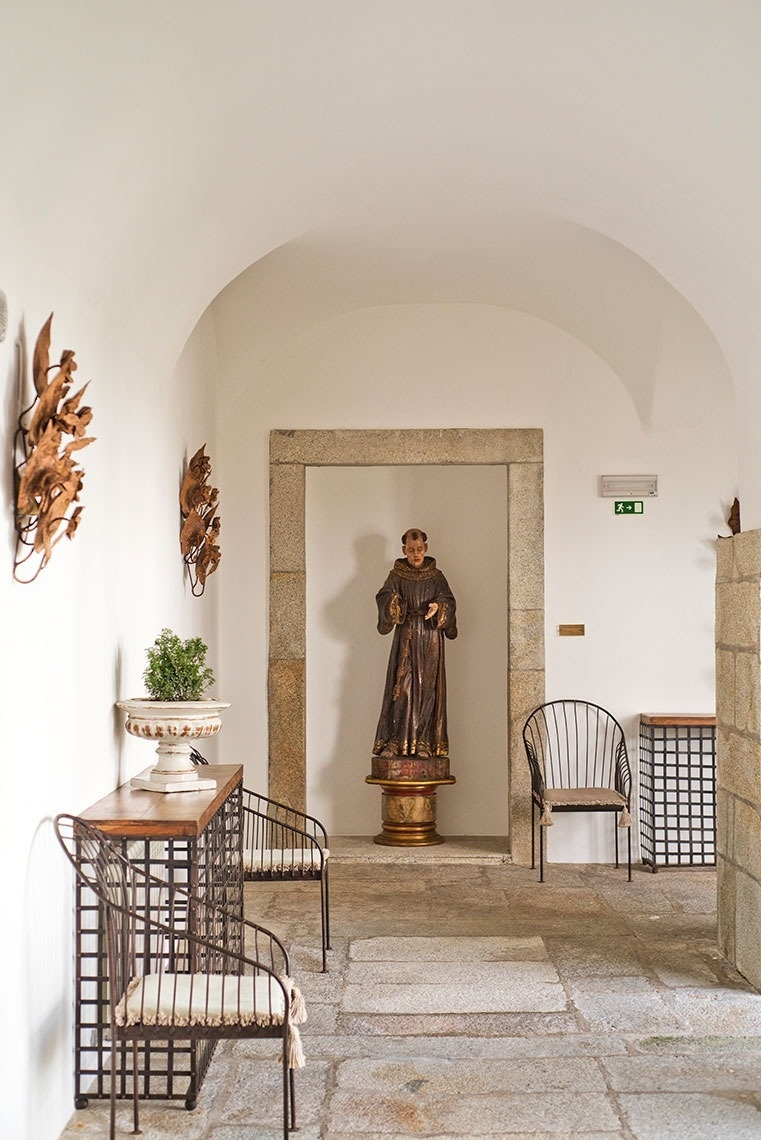 Interior del Lam Hotel Convento do Desagravo con estatua de monje y muebles de hierro forjado.