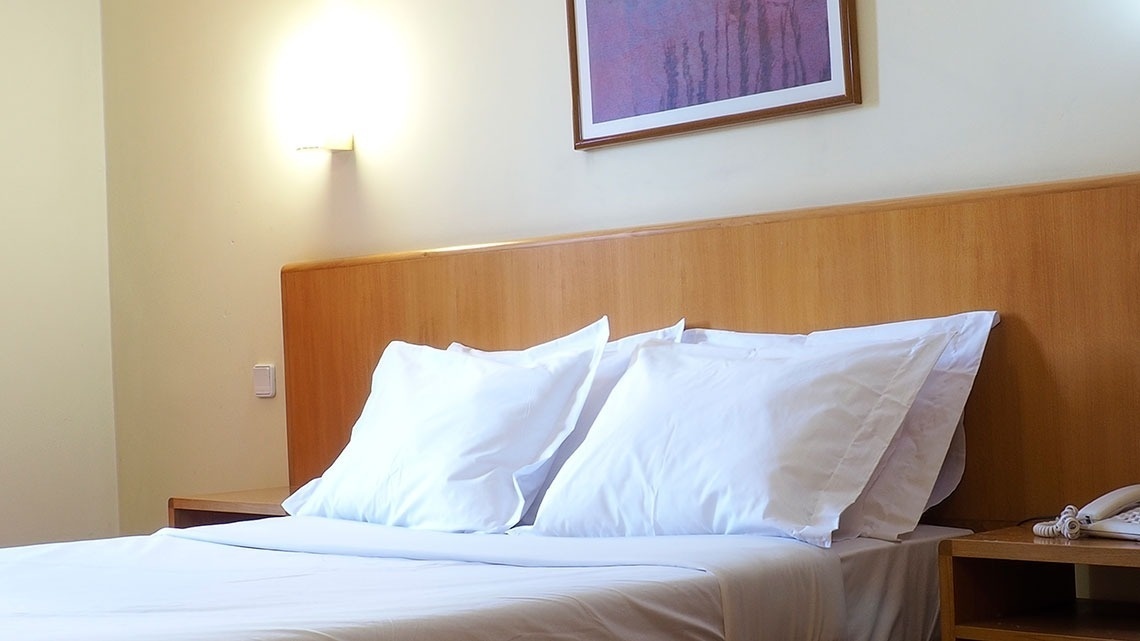 Cama arrumada com travesseiros brancos no Flag Hotel Porto-Maia. Conforto e tranquilidade garantidos.