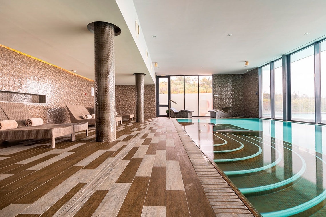 Piscina interior aquecida com espreguiçadeiras no Monchique Resort & SPA by Flagworld Hotels.