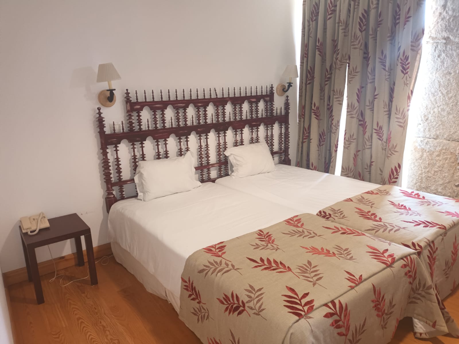 Quarto duplo com cabeceira em madeira escura, lençóis brancos e mantas com padrão de folhas paraLam Hotel Convento do Desagravo.