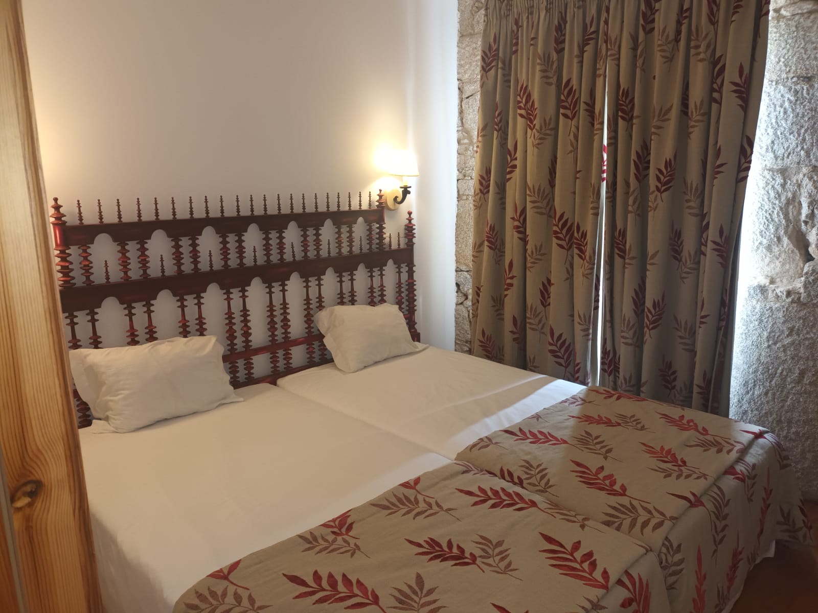 Quarto de hotel com duas camas individuais, cabeceiras de madeira decoradas e cortinas com padrão de folhas. Lam Hotel Convento do Desagravo