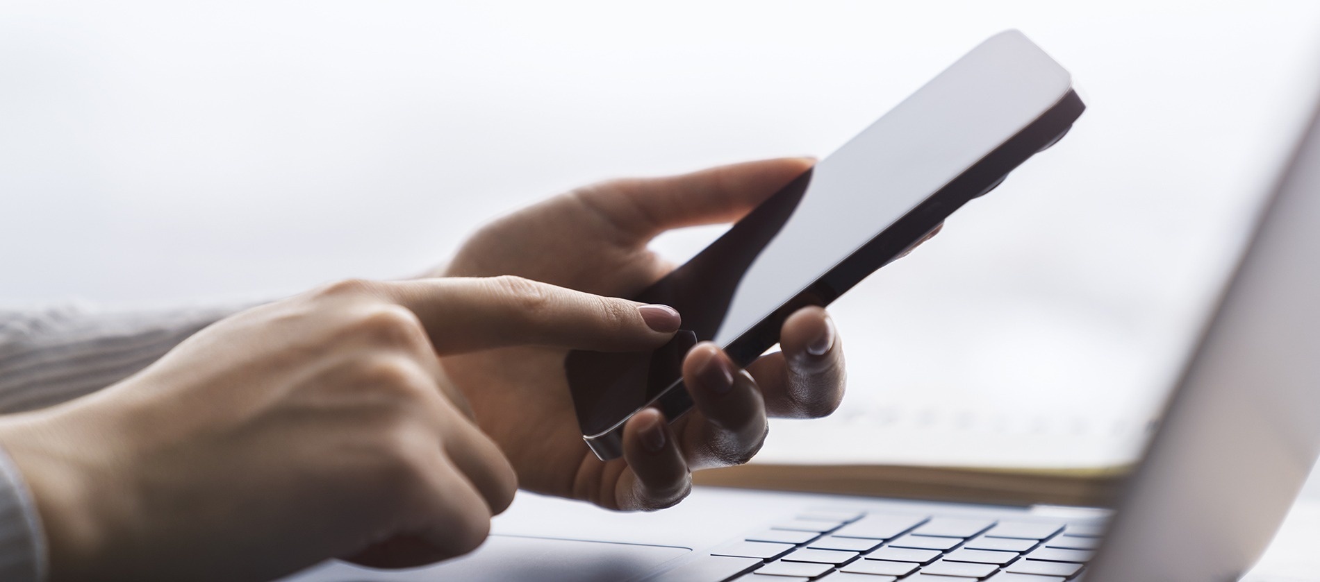 una mujer sostiene un teléfono inteligente frente a una computadora portátil