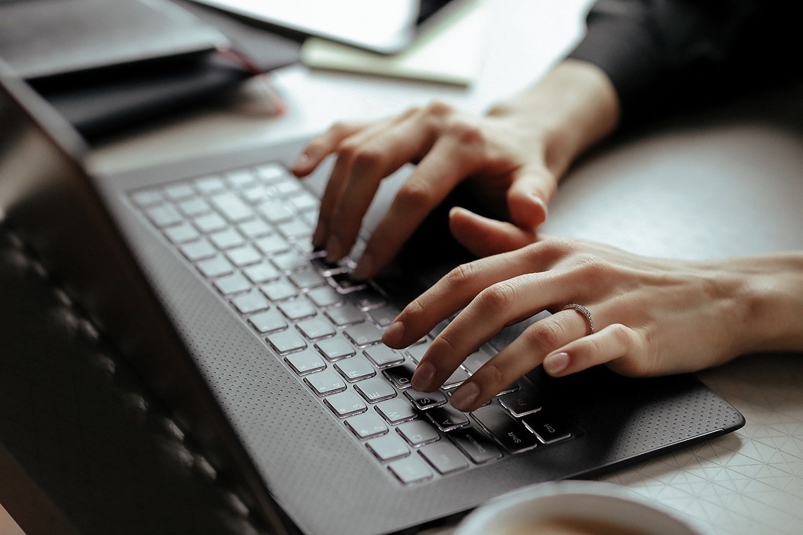 a person is typing on a laptop with a ring on their finger