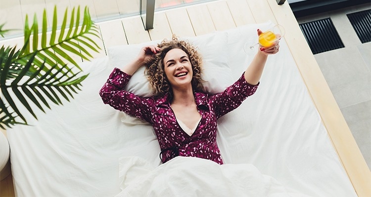 a woman laying on a bed holding a glass of orange juice