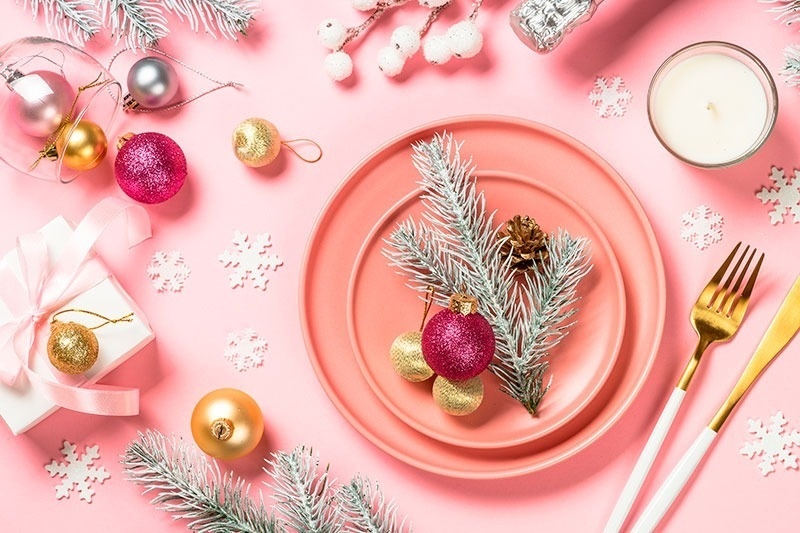 un plato rosa está rodeado de decoraciones navideñas y cubiertos