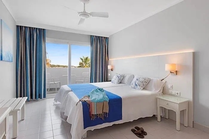 a hotel room with two beds , a ceiling fan and a balcony .