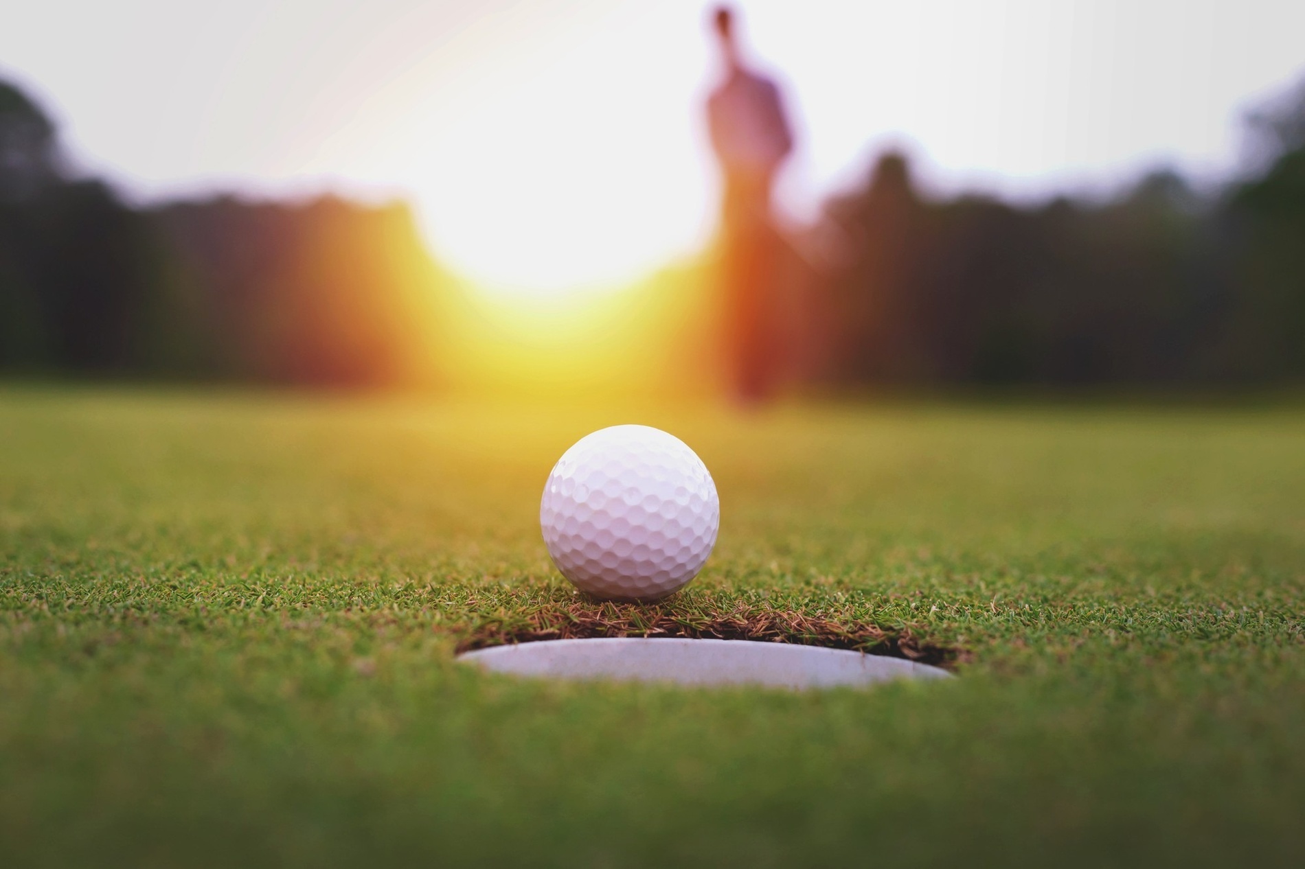 una pelota de golf se sienta en el borde de un agujero al atardecer