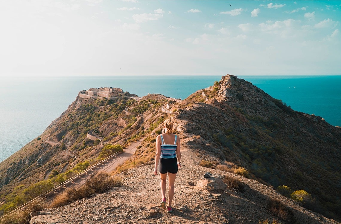 a woman is standing on top of a mountain overlooking the ocean .