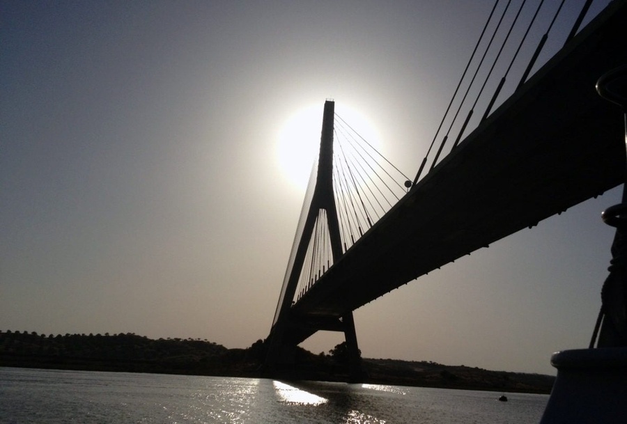 o sol brilha através de uma ponte sobre um corpo de água