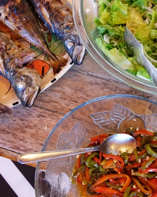 A imagem mostra uma refeição composta por peixe grelhado, salada verde e pimentões cozidos, disposta sobre uma mesa de madeira.