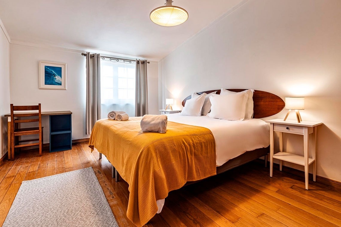 Um quarto luminoso e aconchegante com uma cama grande, chão de madeira e uma área de trabalho junto à janela.