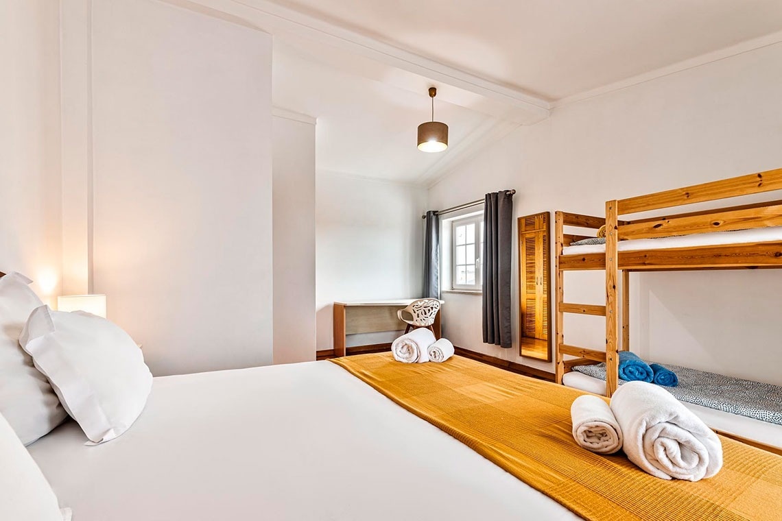 Um quarto de hóspedes moderno e espaçoso com uma cama de casal, um beliche de madeira e uma secretária junto à janela.