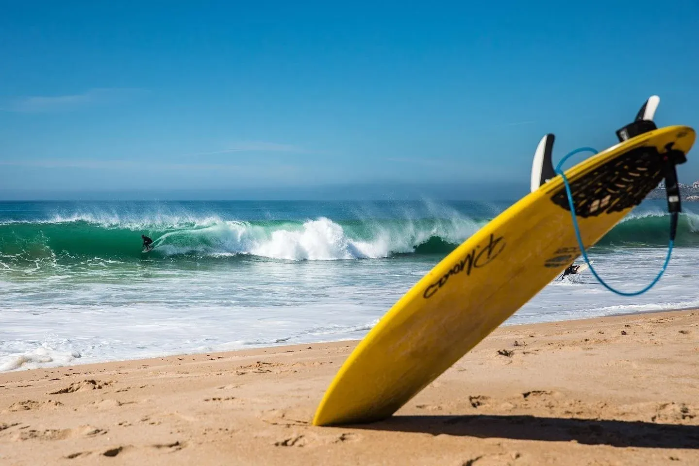 Mulher surfando em onda com prancha amarela e roupa preta. FreesurfCamp