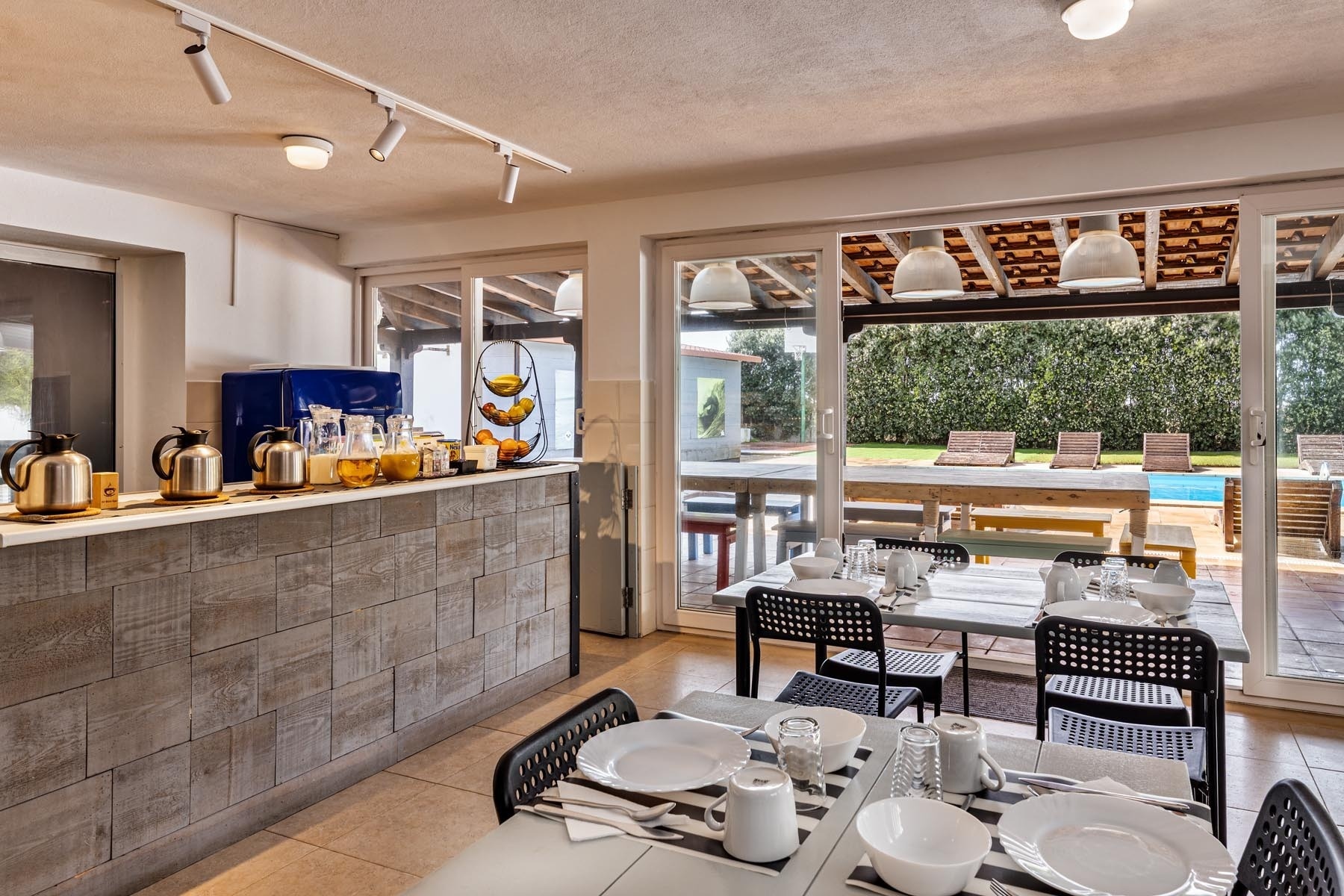 Uma mesa posta com um farto café da manhã para duas pessoas, incluindo ovos, pães, frutas, café, suco e cereais, sobre um jogo americano listrado.