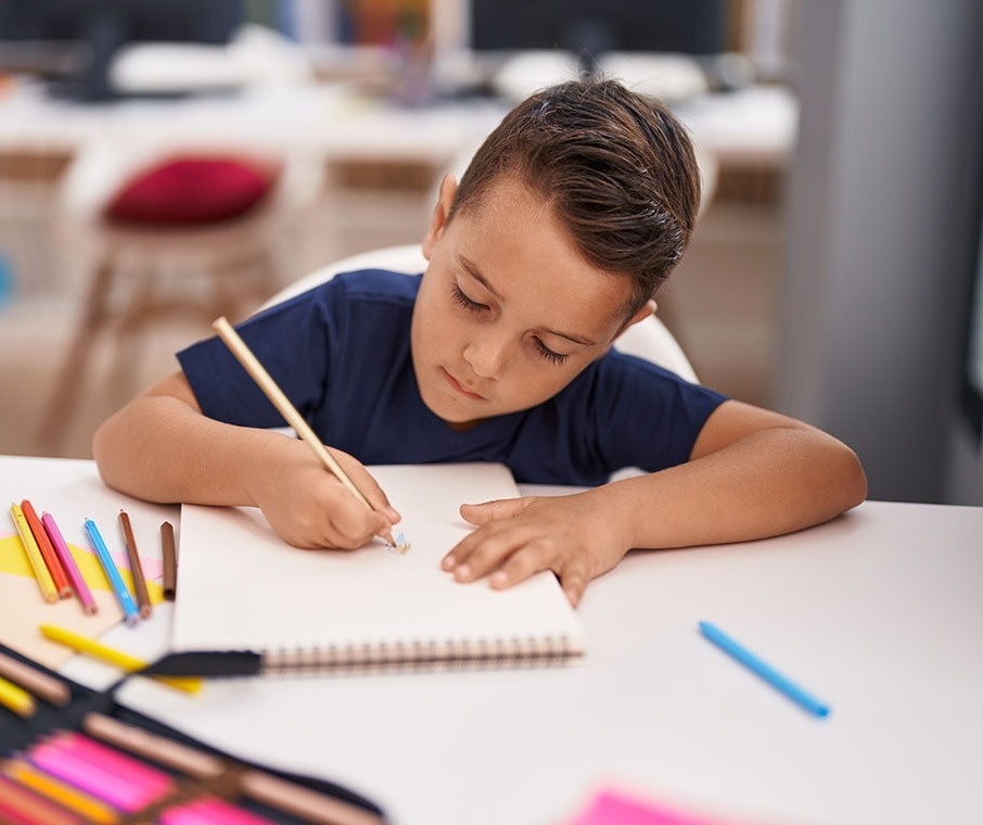 un niño dibuja con un lápiz en un cuaderno