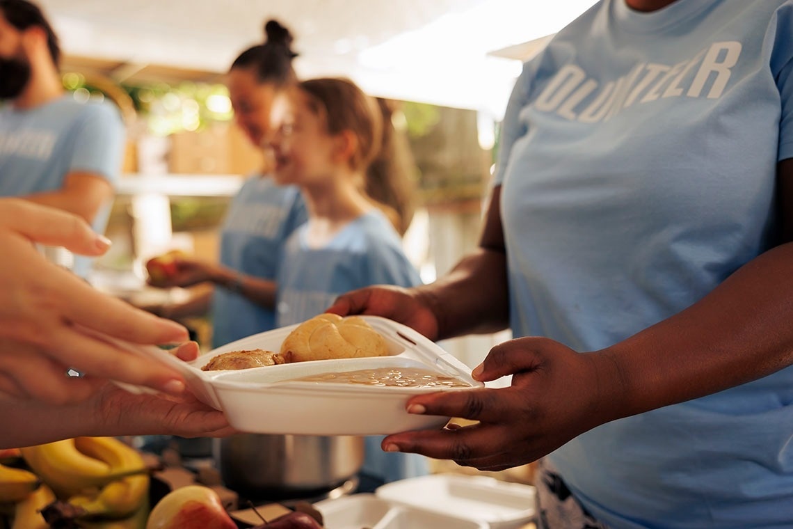 una mujer con una camisa azul con la palabra volunter en ella recibe un plato de comida