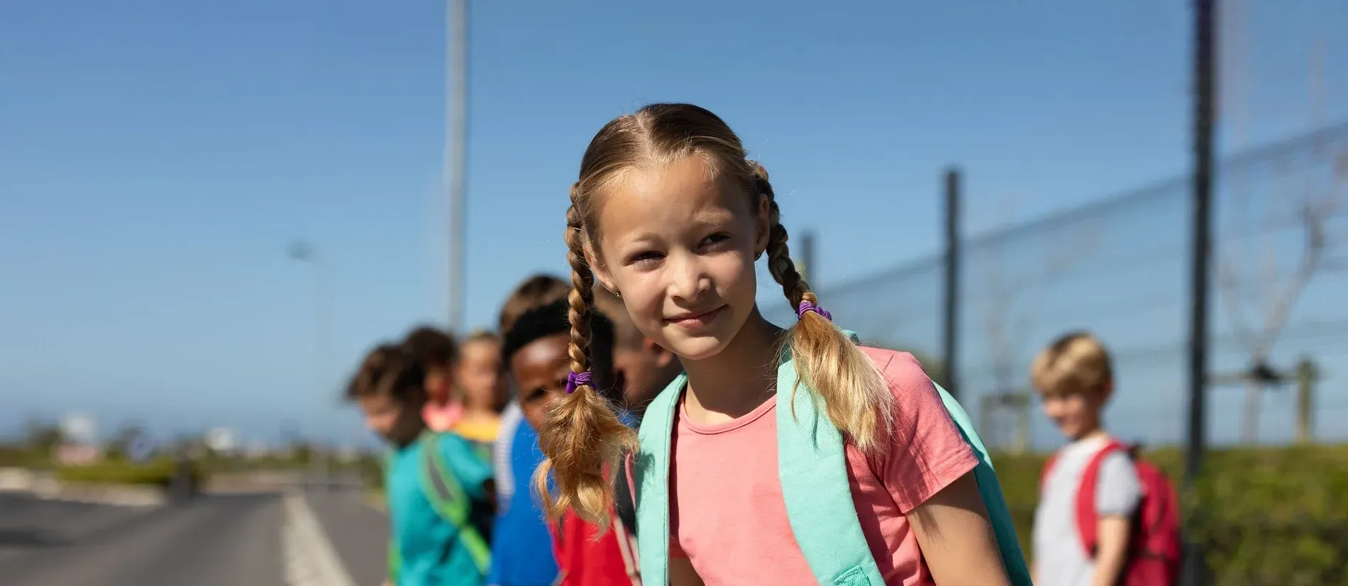 Sobre nosotros, conócenos: Niños felices con mochilas esperan en un día soleado.