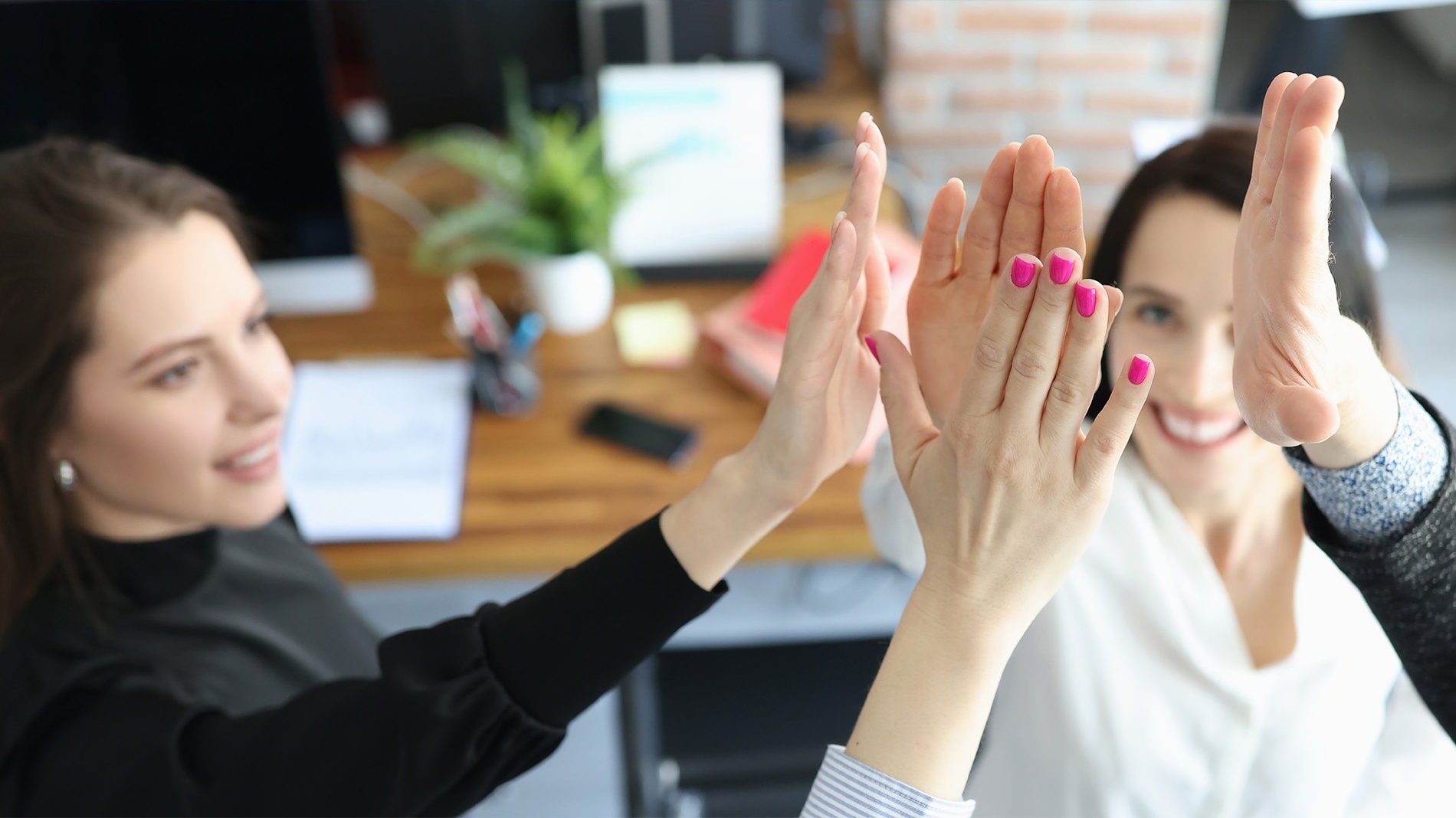 three women with pink nails give each other a high five