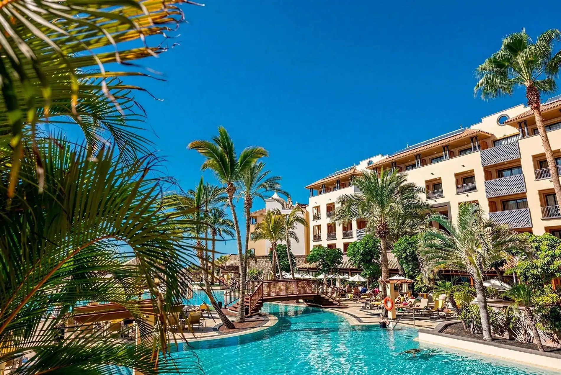Resort todo incluido GF Gran Costa Adeje: piscina, palmeras y sol radiante.