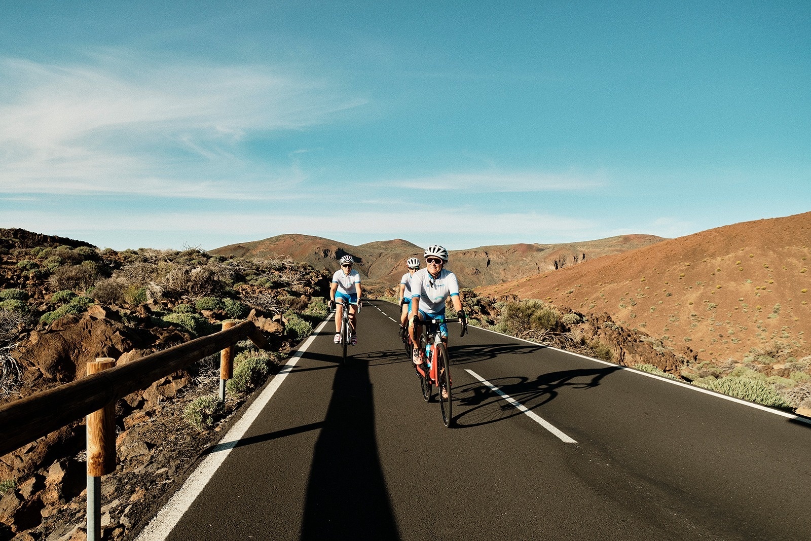 tres personas en bicicleta por una carretera con montañas en el fondo