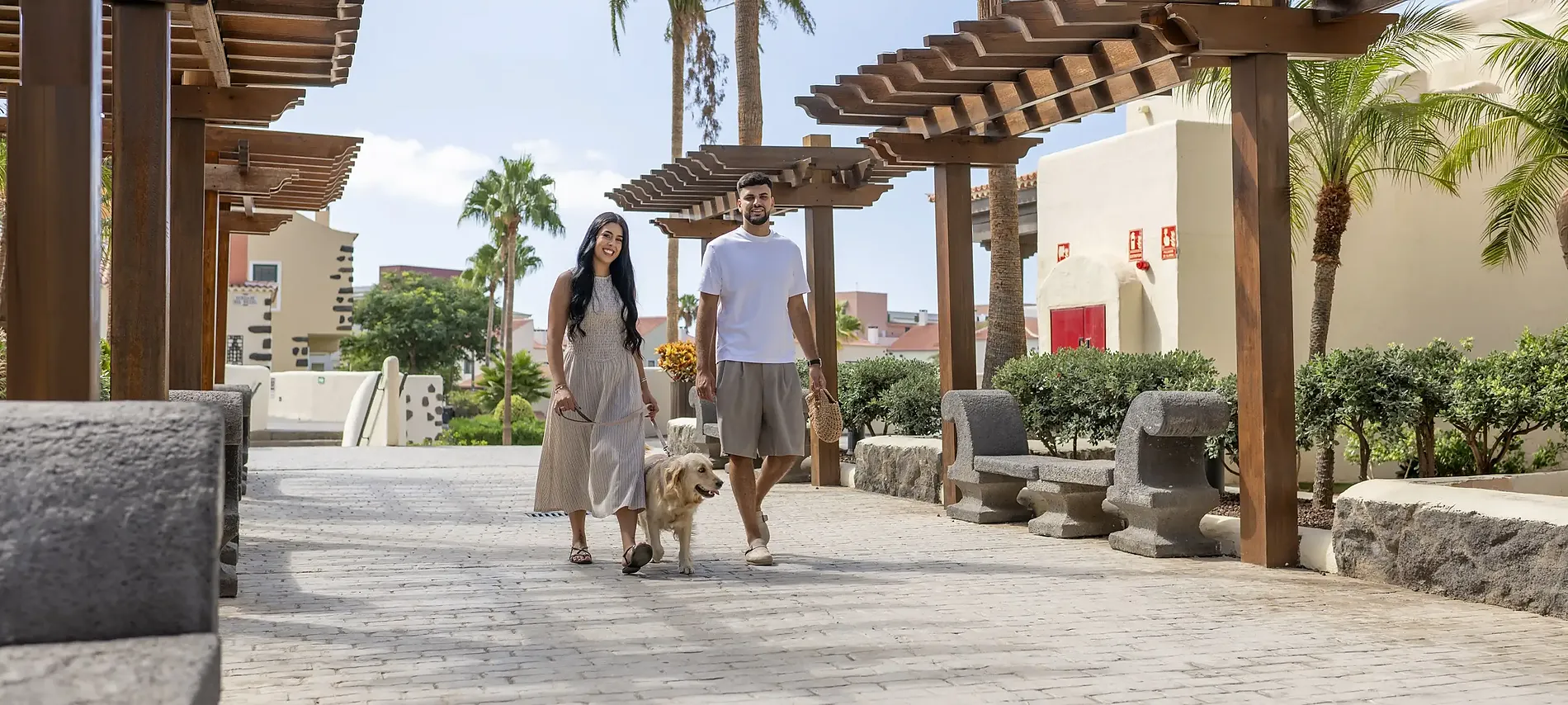 Pareja joven paseando con perro bajo pérgola de madera en hotel GF Isabel