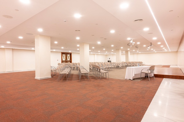 Sala de eventos corporativos con sillas, mesas y escenario.