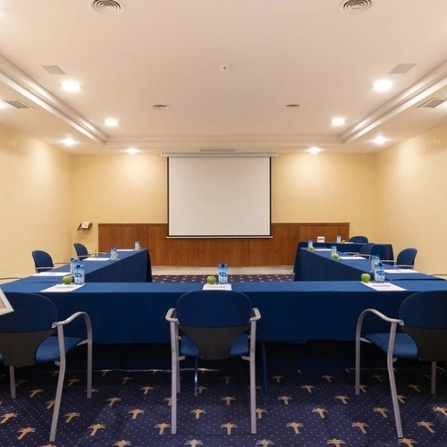 una sala de conferencias con mesas y sillas y una pantalla