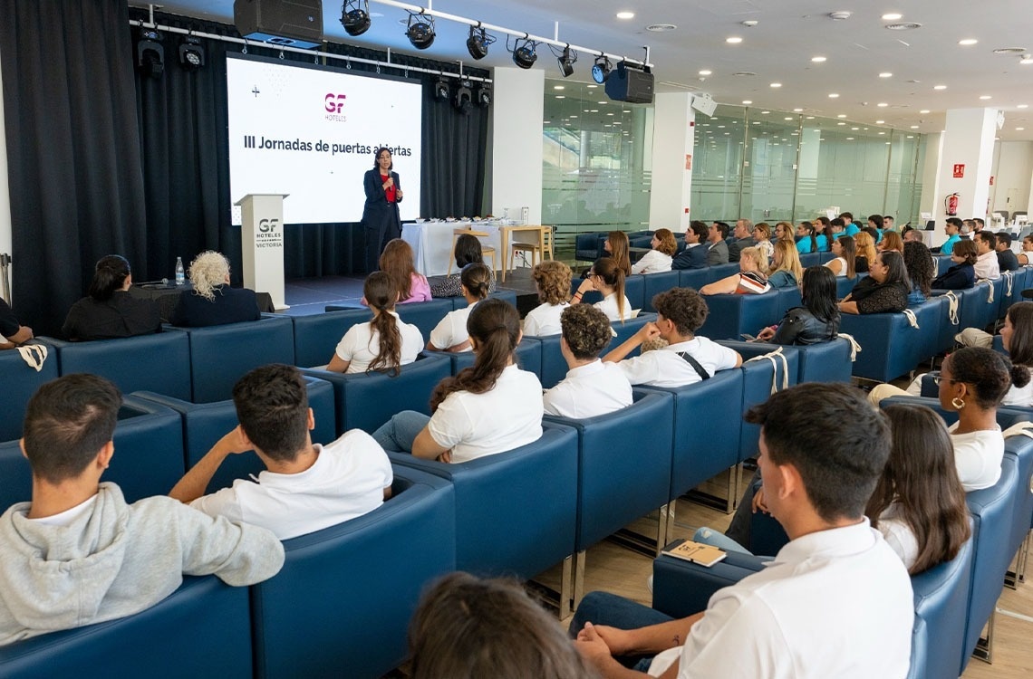 un grupo de personas se sienta en un auditorio frente a una pantalla que dice iii jornadas de puertas abiertas