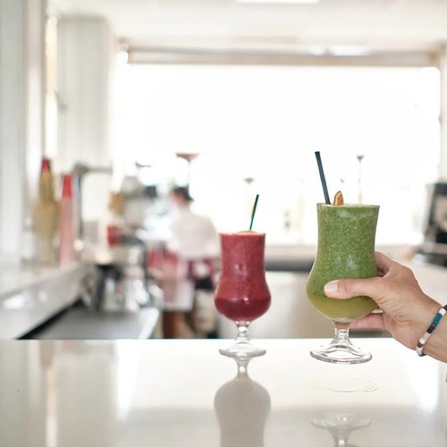 a person holding a green smoothie next to a red smoothie