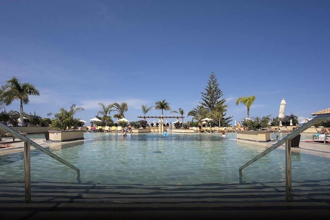 una piscina rodeada de sillas y sombrillas con vistas al océano